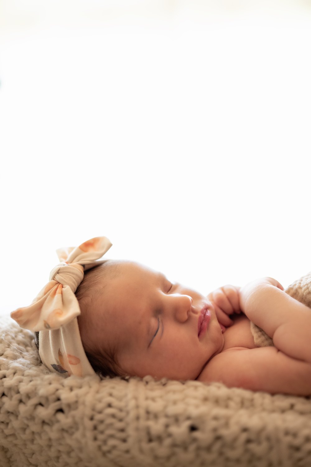 A sleeping newborn wearing a soft floral bow